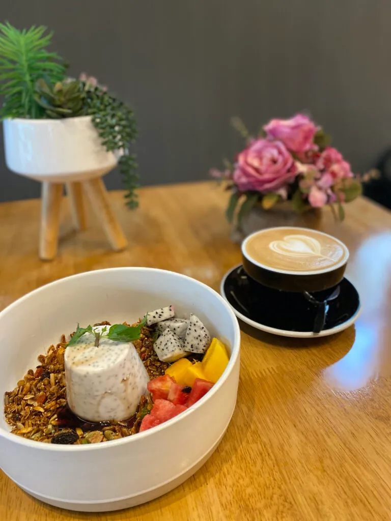 Set chia pudding on a bed of granola and tropical fruit next to a latte with heart shaped latte art at Poached Breakfast Cafe, Chalong, Phuket