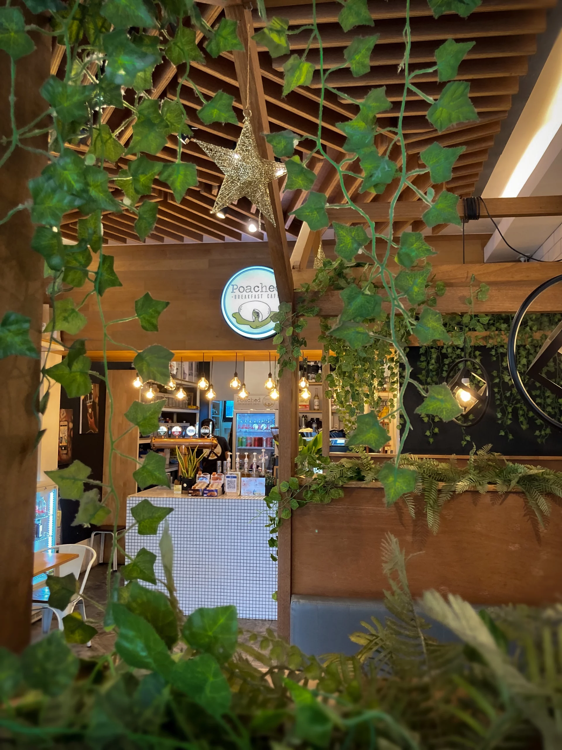 A photograph of the Poached Breakfast Cafe Sign over the coffee bar, framed by some green foliage at Poached Breakfast Cafe, Chalong, Phuket, Thailand - the best cafe in Phuket