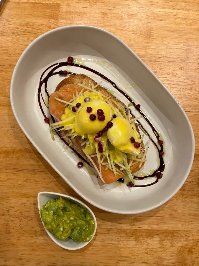 Smoked Salmon Eggs Benedict topped with pomegranate seeds and a balsamic drizzle next to some smashed avocado at Poached Breakfast Cafe, Chalong, Phuket. The best breakfast in Phuket!