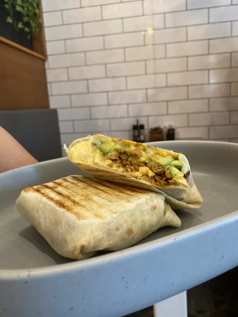A server holding a plate with a grilled breakfast burrito filled with scrambled eggs, avocado, sausage and monterey jack cheese at the best lunch cafe in Chalong, Poached Breakfast Cafe, Chalong, Phuket, Thailand