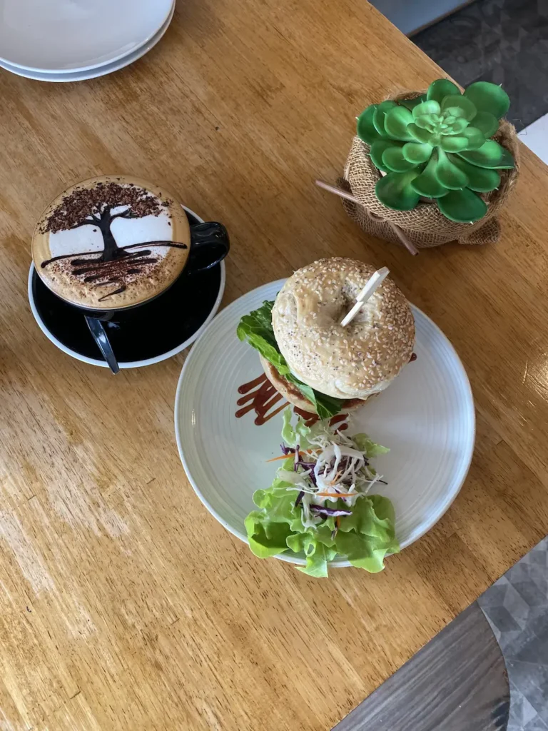 Coffee with a tree drawn in the top of the coffee and a halloumi bagel on a table next to a succulent plant at the place with the Best Coffee Art Phuket Has to Offer: Poached Breakfast Cafe, Chalong, Phuket, Thailand