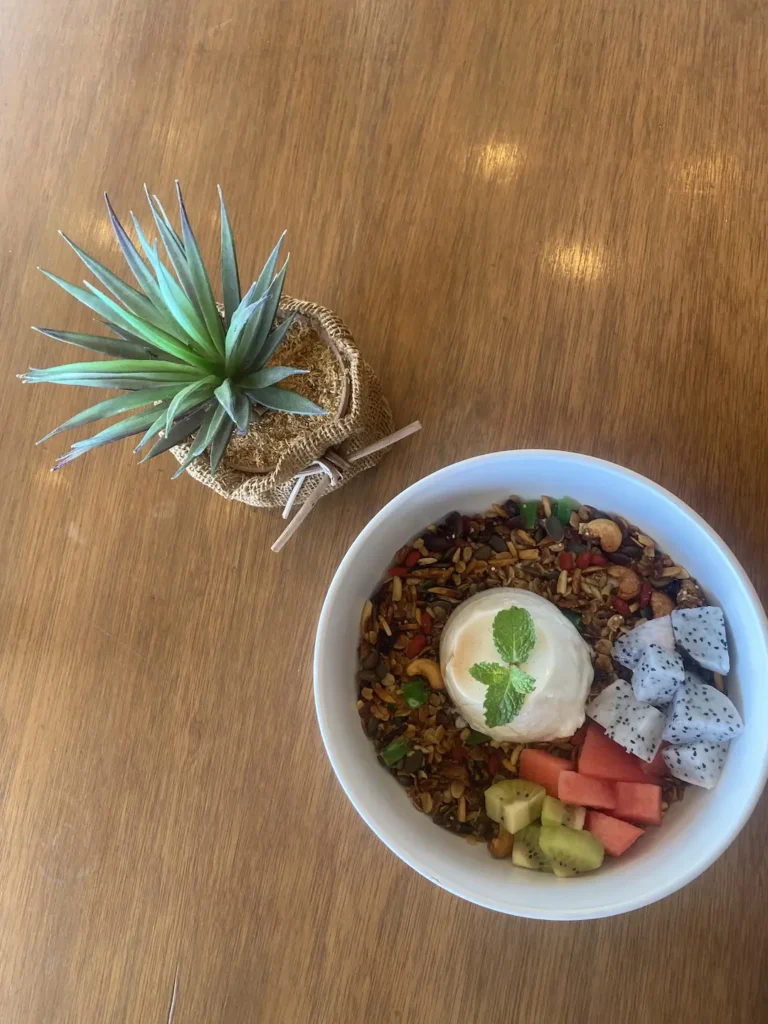 Breakfast panna cotta with hazelnut praline, surrounded by granola and fresh fruit in a large bowl next to a succulent. A pretty good alternative to a breakfast burrito in Chalong at Poached Breakfast Cafe, Chalong, Phuket, Thailand