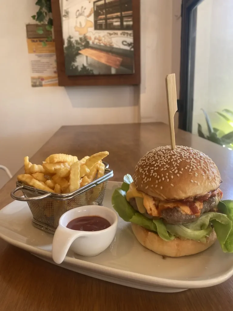 Spicy beef burger with cheese, ketchup and a basket of fries on a table. A good alternative to a breakfast burrito in Chalong at Poached Breakfast Cafe, Chalong, Phuket, Thailand