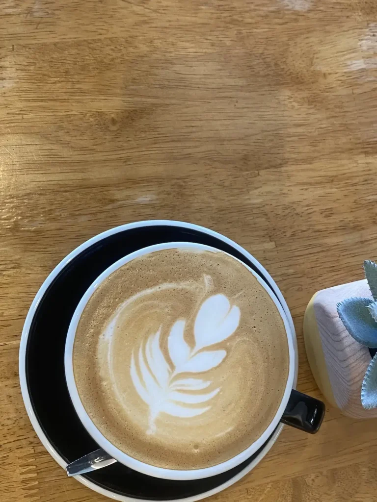 Latte with latte art of a leaf in a cup and saucer on a wooden table. Only at the spot with the best juice near Chalong - Poached Breakfast Cafe, Chalong, Phuket, Thailand