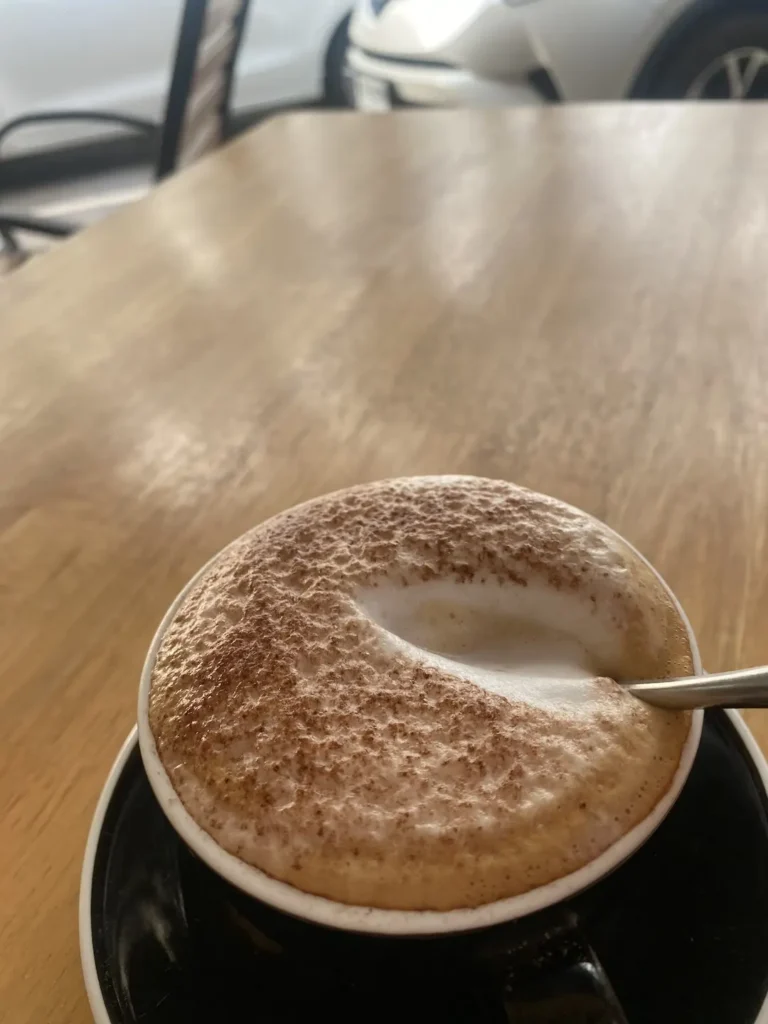 A spoon breaking into the foam on the top of a cappuccino on a table. The best thing to drink before a day of island hopping in Phuket.